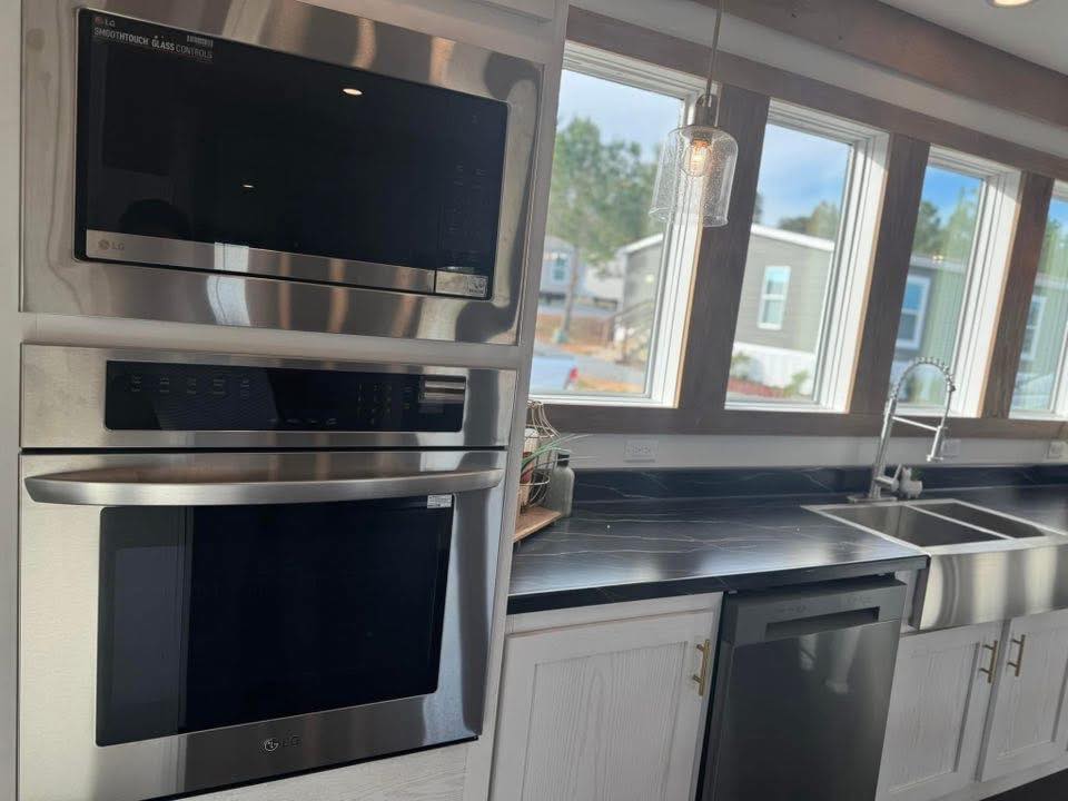 Modern kitchen with stainless steel oven and microwave. A sleek black countertop and large sink are illuminated by natural light from four windows.