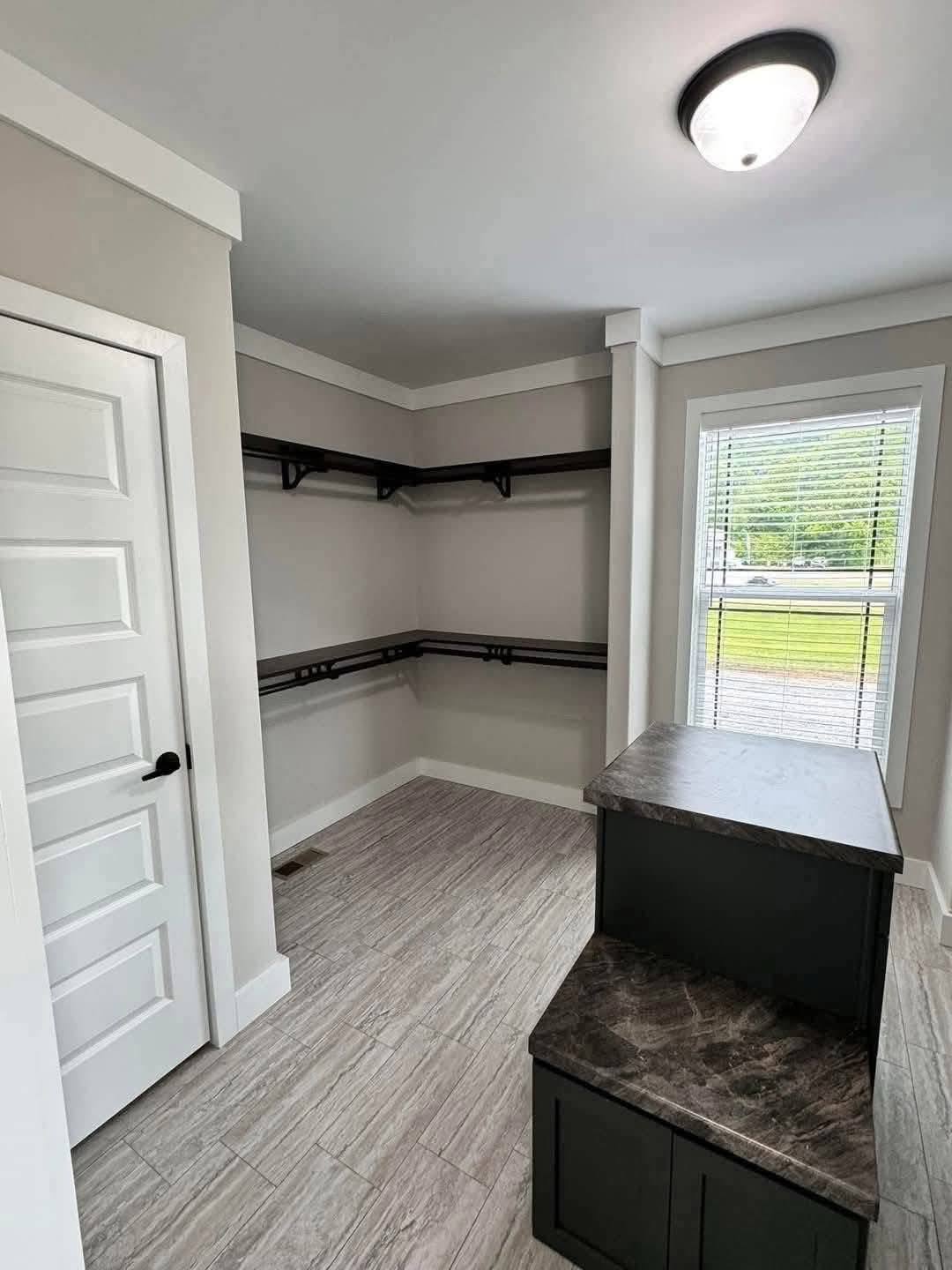 Walk-in closet with light gray walls and tiled floor, featuring dark wood shelves along two walls. A small window offers natural light.