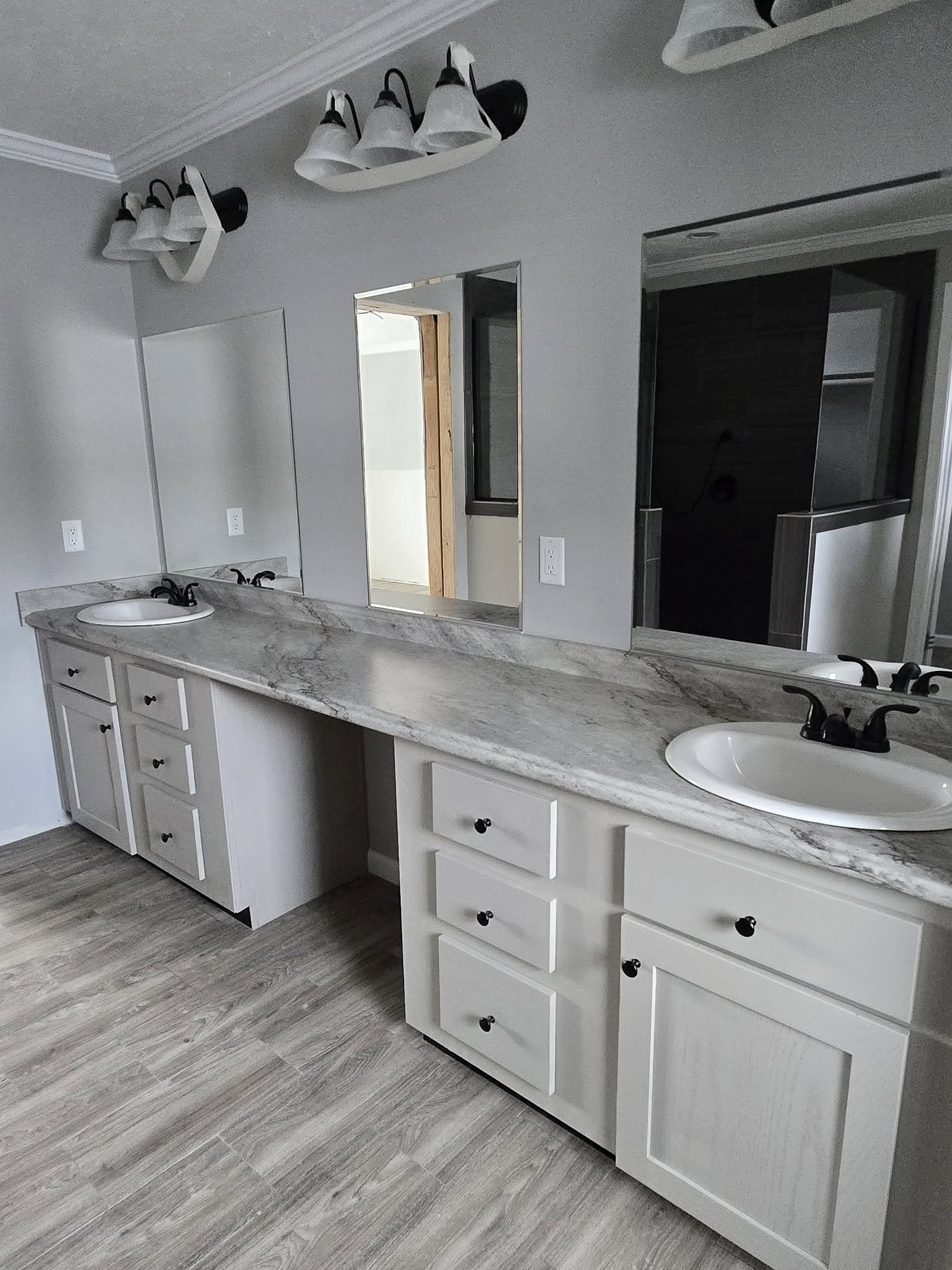Bright bathroom with two white sinks set in a long marble countertop. Dual rectangular mirrors, modern black faucets, and overhead light fixtures accentuate the sleek, minimalist design.