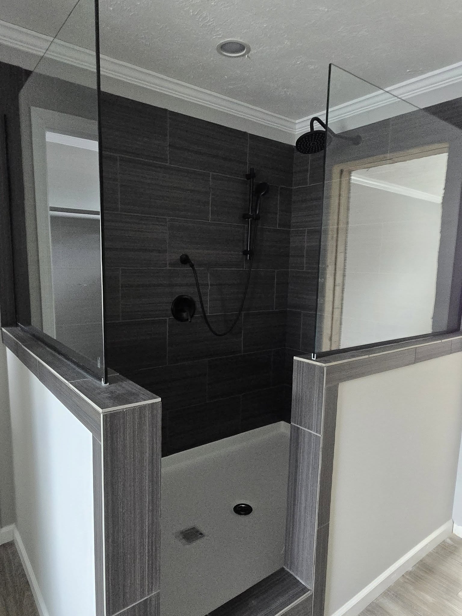 Modern shower with dark gray textured tiles, partial glass walls, and a black showerhead. The space is clean and minimalist in design.