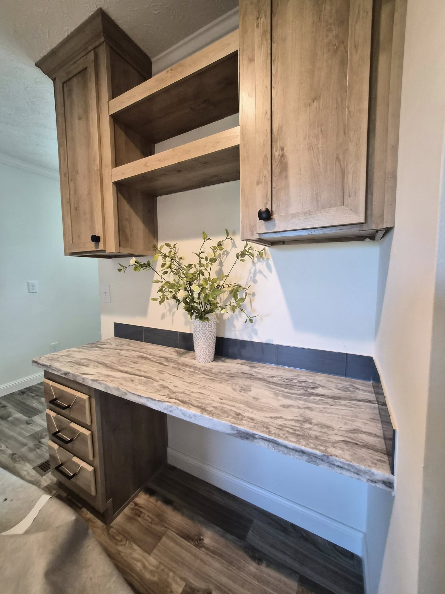 Wooden cabinets with a gray countertop and drawers below. A vase with green foliage adds a fresh touch, resting against a light wall in a cozy setting.