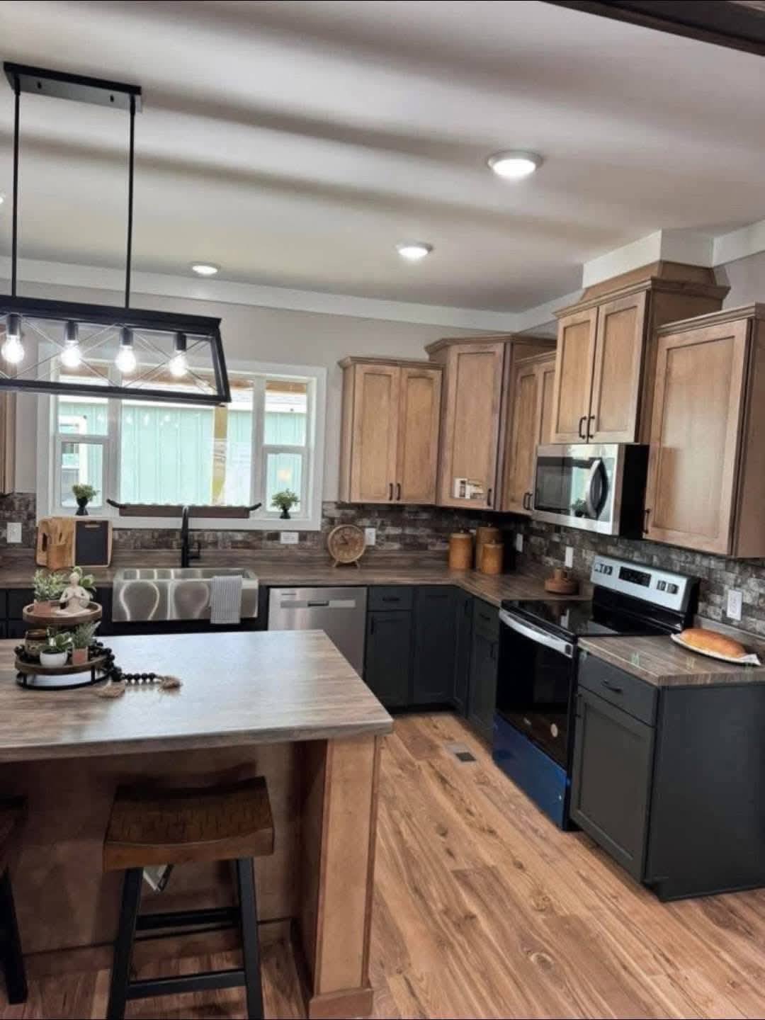 Modern kitchen with wood cabinets, black appliances, and a farmhouse sink. Central island with stools and pendant lighting. Warm, inviting atmosphere.