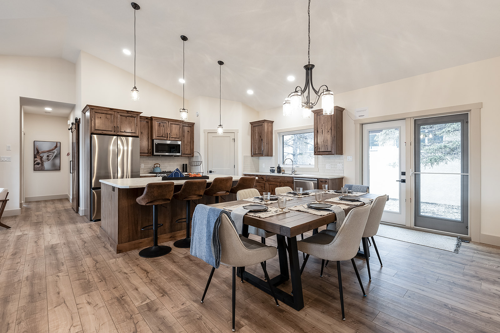 Spacious kitchen and dining area with wood floors, rustic cabinets, and modern fixtures. A set table and cozy ambiance create a welcoming atmosphere.