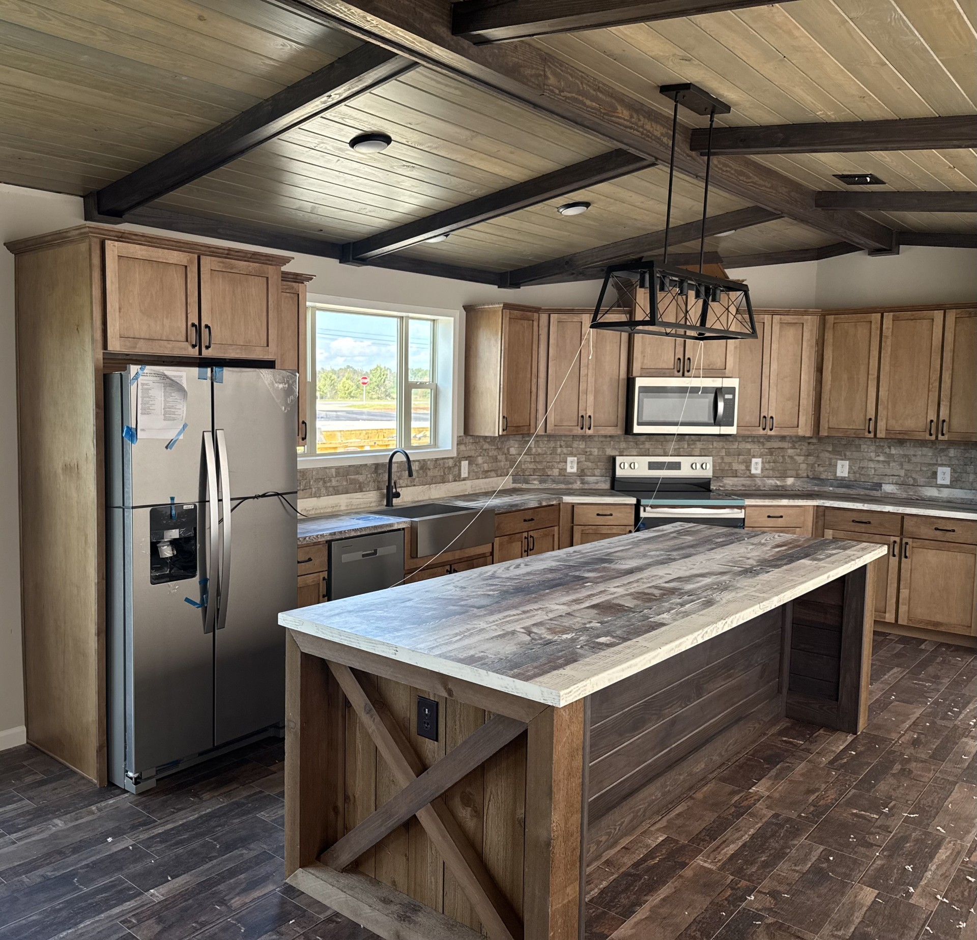 Spacious kitchen with wooden beams, a large island, stainless steel appliances, and rustic cabinets. A window lets in natural light, enhancing warmth.