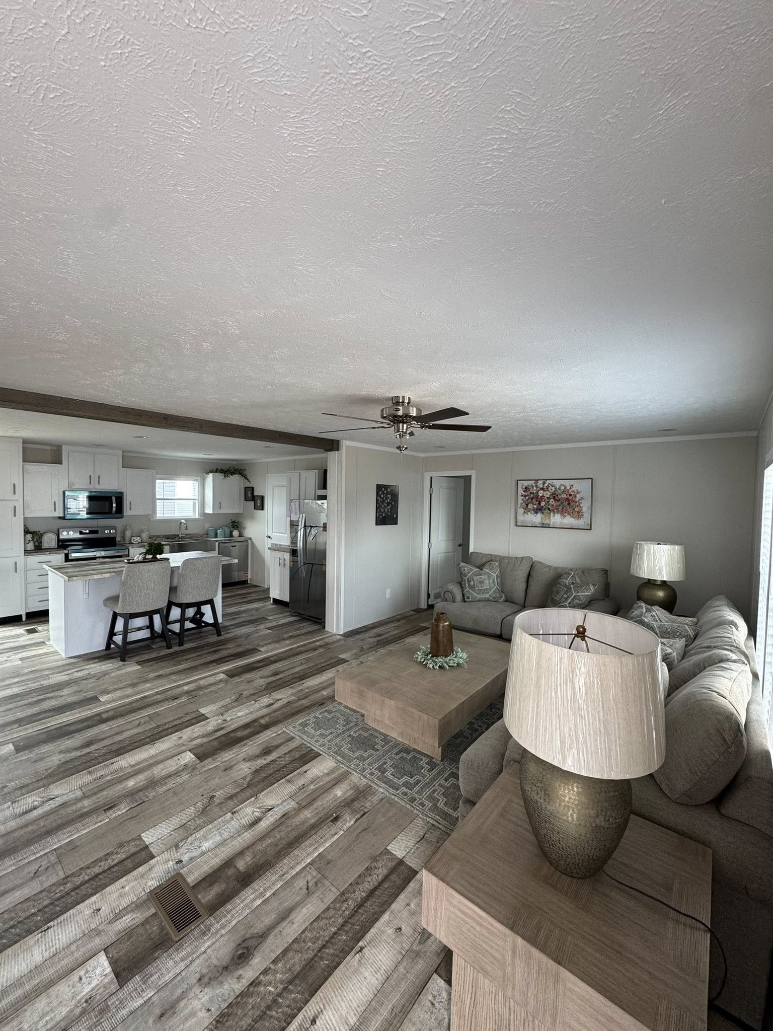 Open-concept living space with a wooden floor, featuring a cozy beige couch, modern kitchen with white cabinets, dining table, and muted decor.
