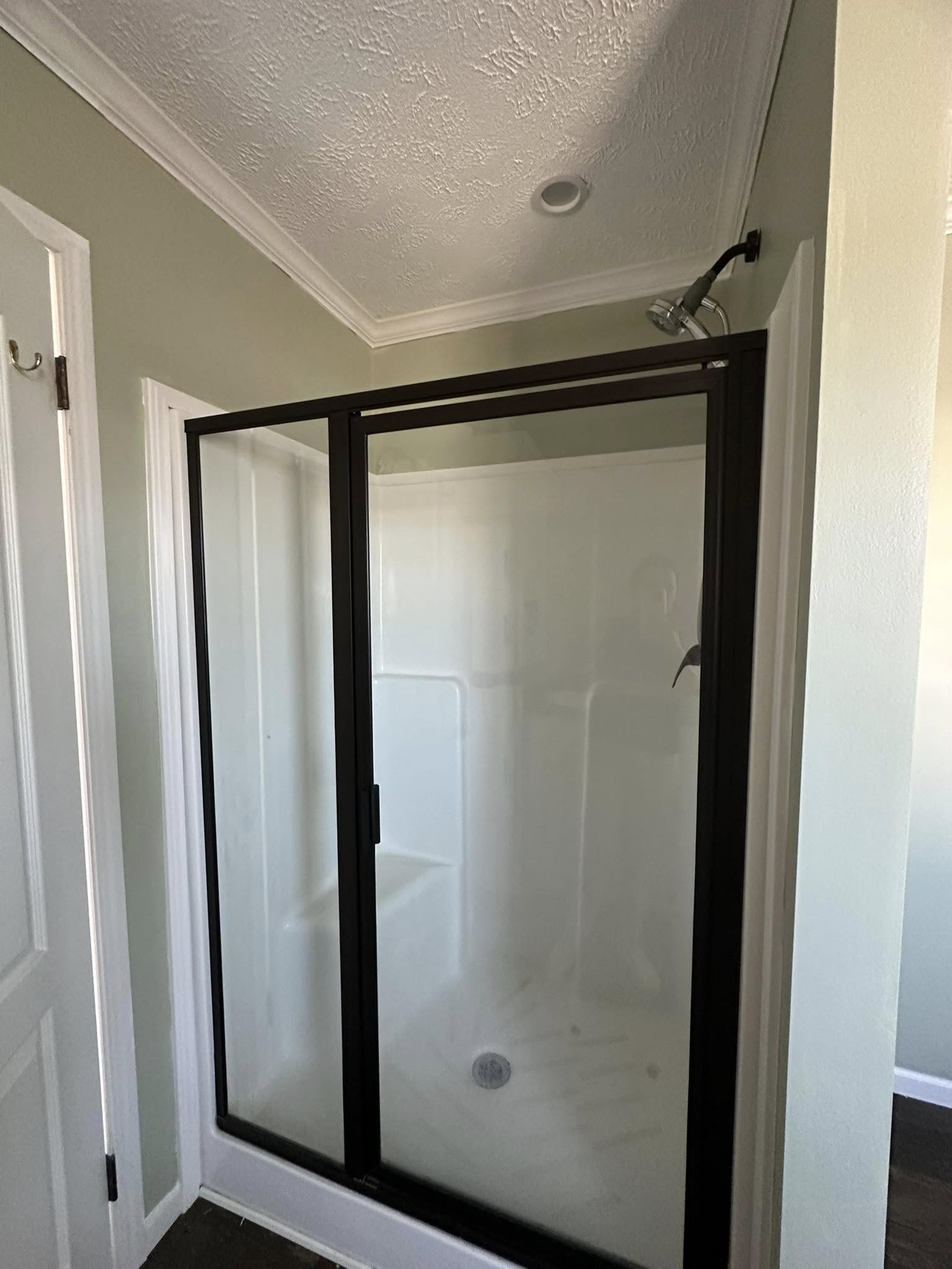 Walk-in shower with frosted glass door and black frame in a bathroom. It has a white interior with a showerhead above, evoking a clean, modern feel.