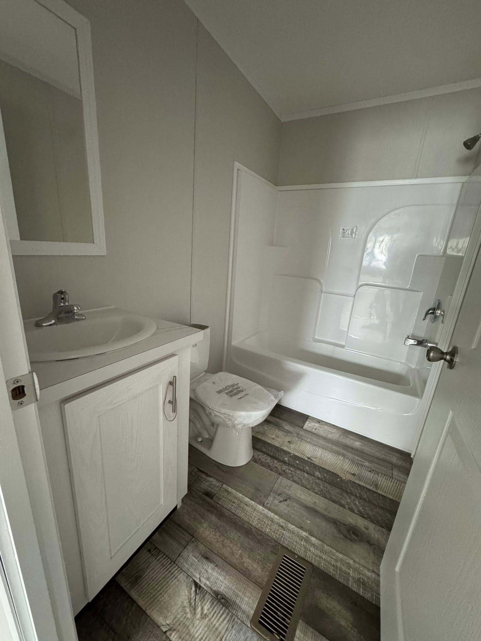 Empty room with light gray walls and rustic wooden flooring. A single window with blinds lets in natural light, creating a calm and spacious atmosphere.
