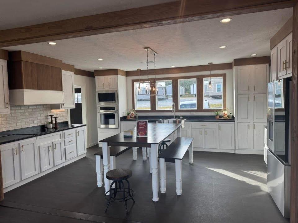 Modern kitchen with white cabinets, wooden beams, and stainless steel appliances. A large island with seating is centered under pendant lights, creating a welcoming and bright atmosphere.