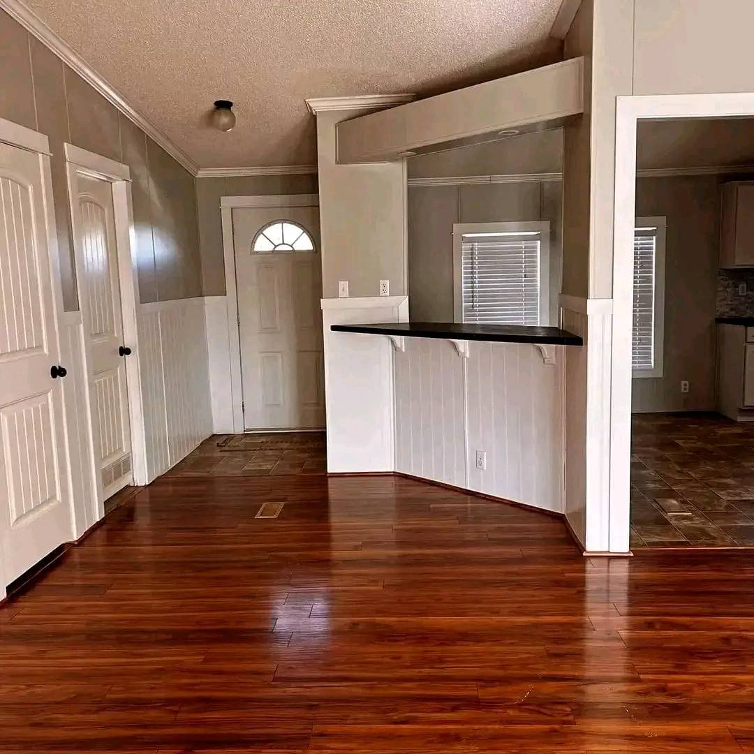 A bright room with polished hardwood floors, white wainscoting, and light gray walls. It features two doors, a window, and a small counter.