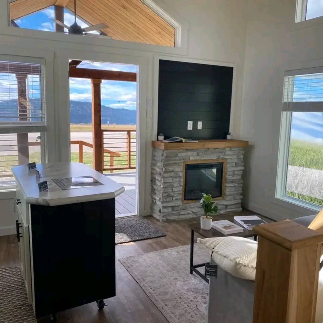 Modern living room with large windows showing a scenic mountain view. Features a stone fireplace, cozy seating, and a small table with decor.
