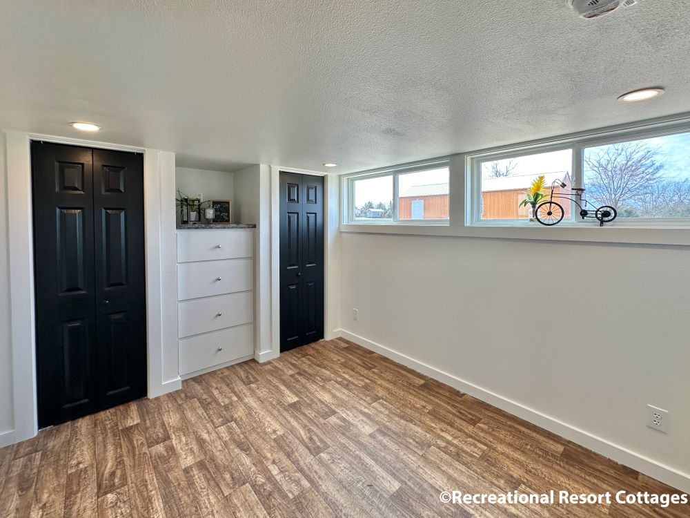 Bright room with wood flooring, white walls, and black double doors. Narrow transom windows bring in natural light. Minimalist decor, cozy ambiance.