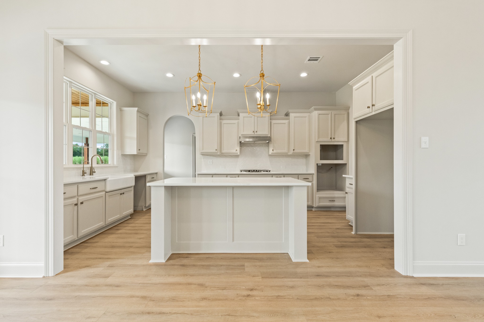 Spacious, light-filled open-plan home interior with a kitchen and living area. Features wood floors, large windows, and elegant chandeliers.