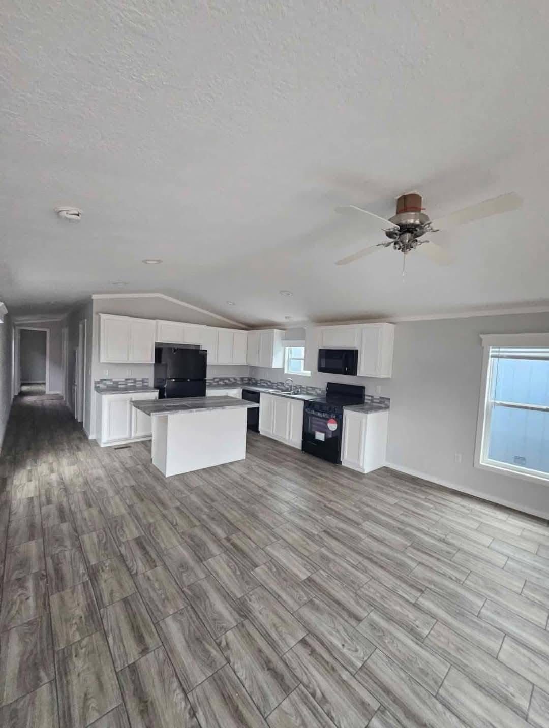 Spacious kitchen with white cabinets, wood-patterned floor, black appliances, and a ceiling fan. Bright and modern with natural light.