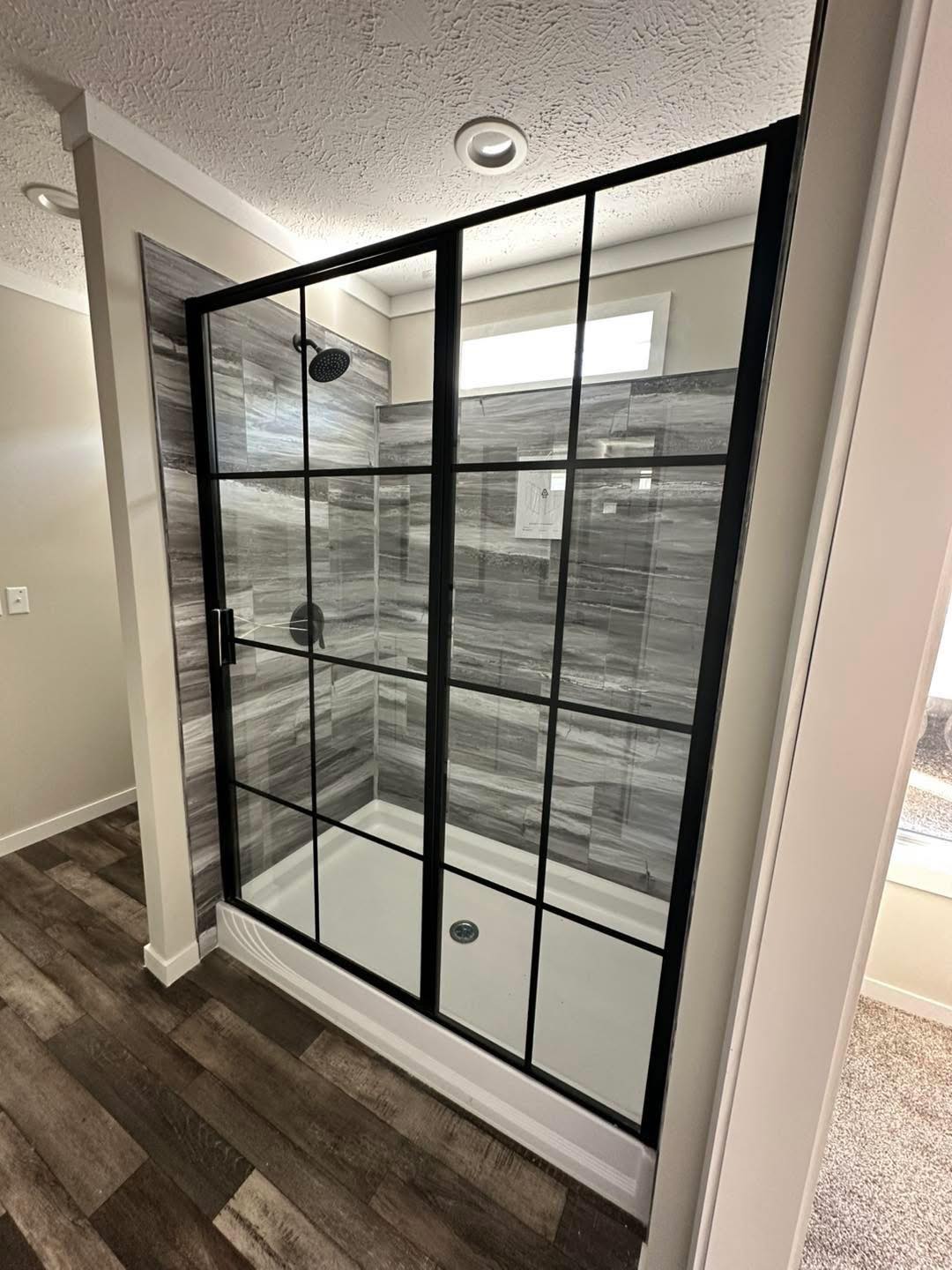 A modern shower with gray tile walls and a black-framed glass door. A rainfall showerhead is visible, set against a sleek, minimalist bathroom design.