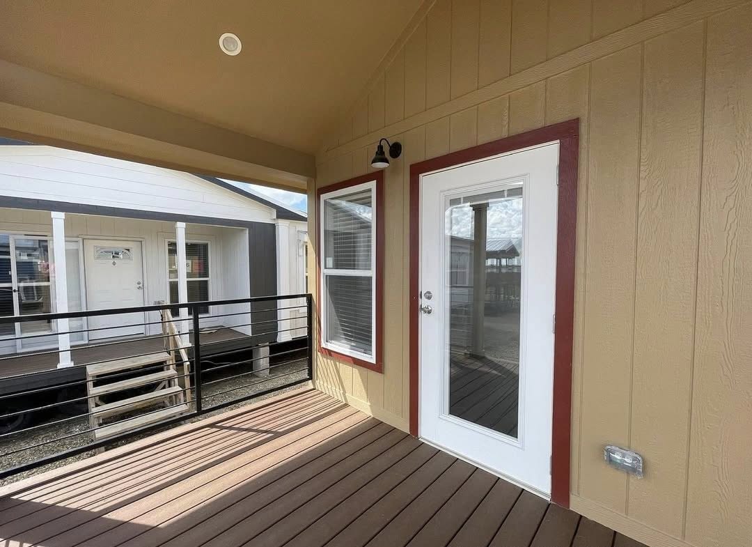 Cozy wooden porch with tan walls and red trim, featuring a white door and window. Overlooked by another house, creating a welcoming atmosphere.