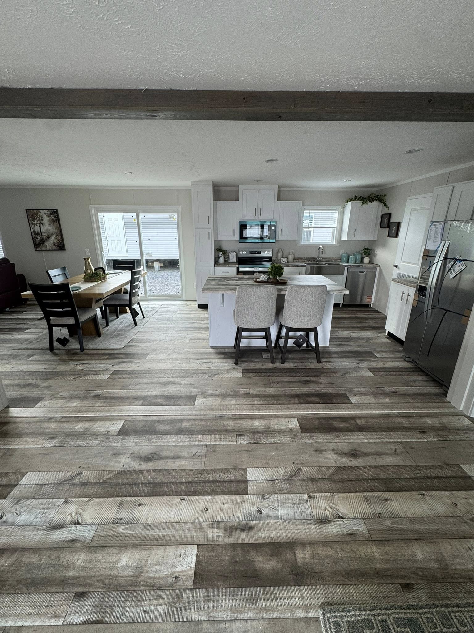 Modern kitchen and dining area with wood flooring and white cabinets. A kitchen island with two chairs faces the stainless steel appliances, creating a cozy, inviting atmosphere.