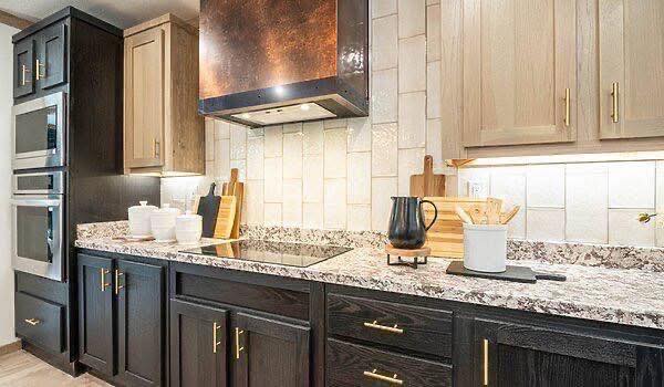 Modern kitchen with dark and light wood cabinets, copper range hood, granite countertops, cutting boards, white jars, and a black kettle.