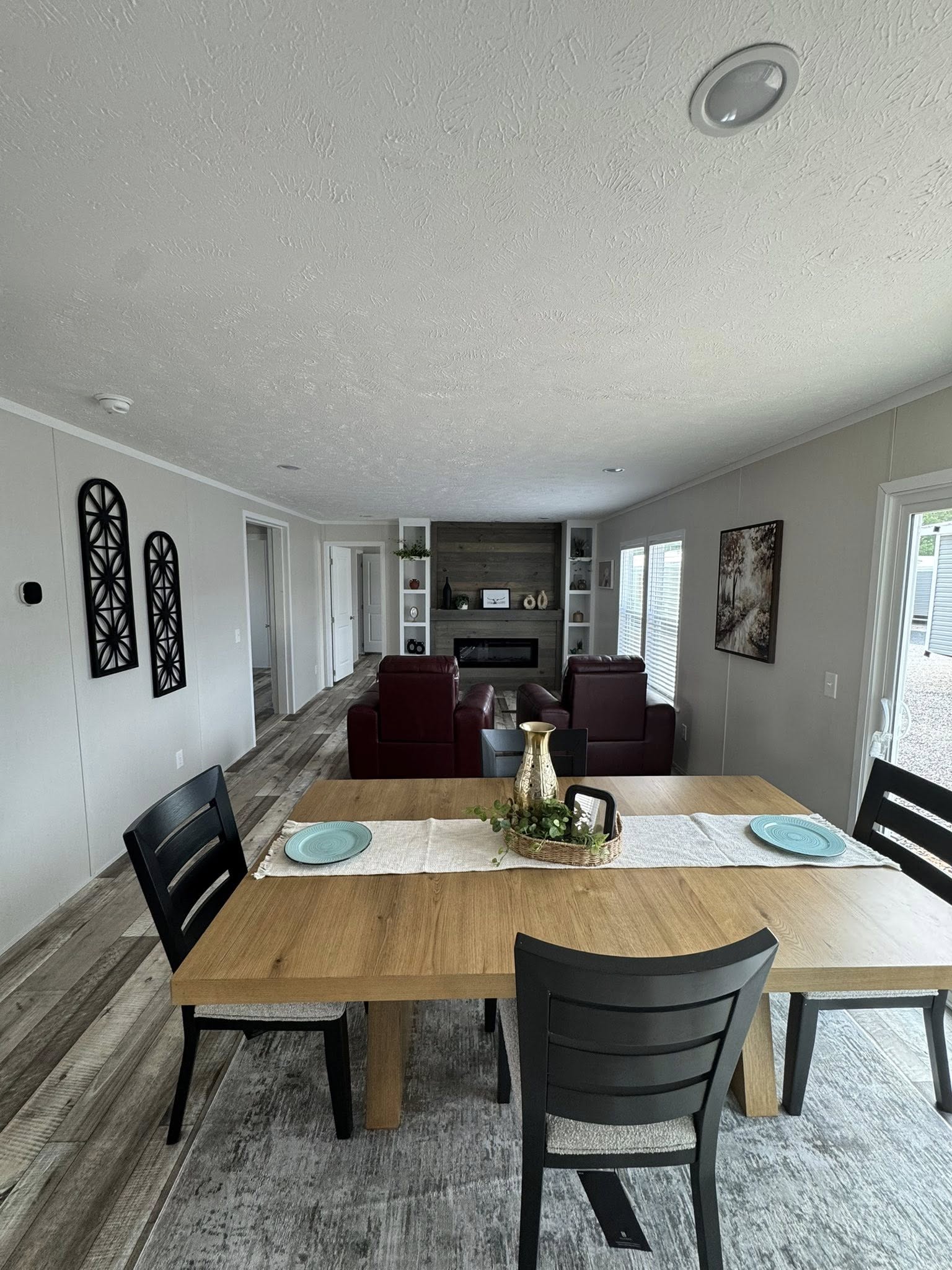 Modern living room and dining area with a wooden table set with blue plates, black chairs, decorative vases. Red chairs face a fireplace and a shelf.