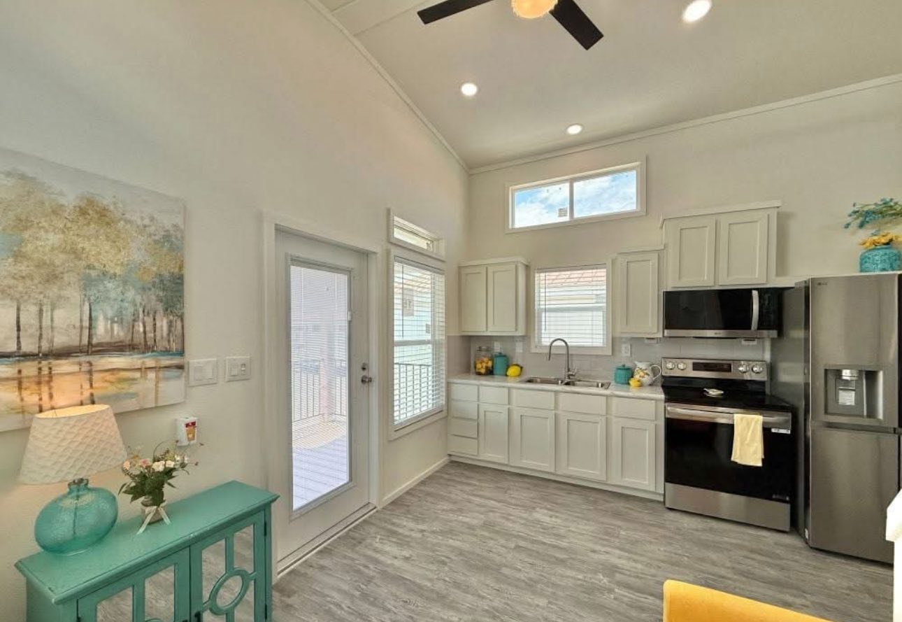 Bright kitchen with modern decor, high ceiling, and natural light. Features white cabinets, stainless appliances, and teal accents for a cheerful ambiance.
