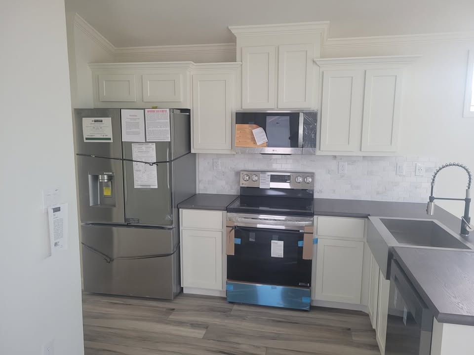 Modern kitchen with light cabinetry and stainless steel appliances. Features include a fridge with documents, electric stove, and a double sink. Bright ambiance.