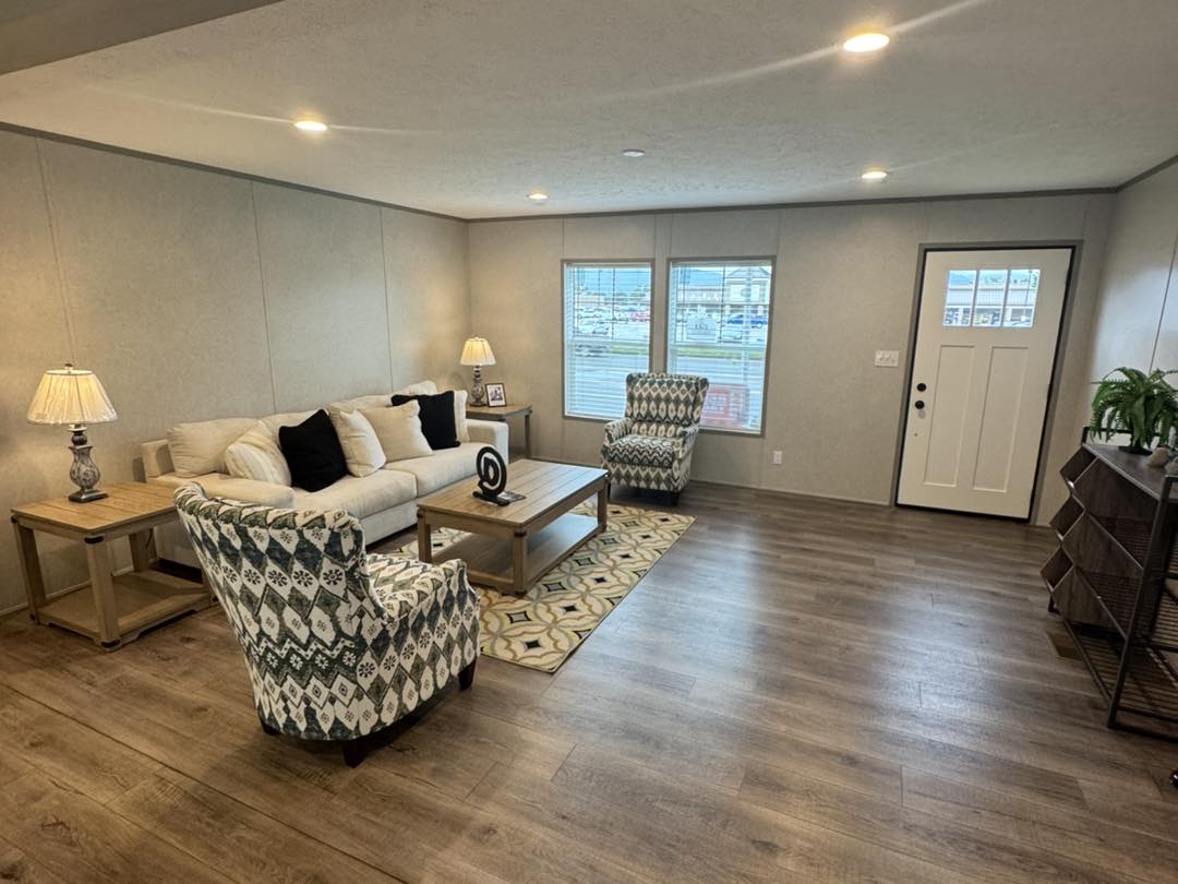 Spacious living room with a cozy beige sofa, patterned armchairs, and wooden tables. Soft lighting enhances the warm, inviting atmosphere.