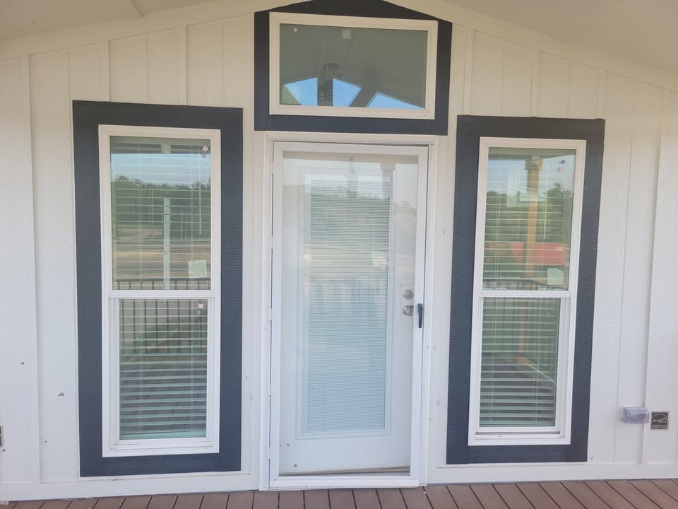A white building exterior with a central glass door flanked by two tall windows, all framed in dark trim, creating a modern and symmetrical design.