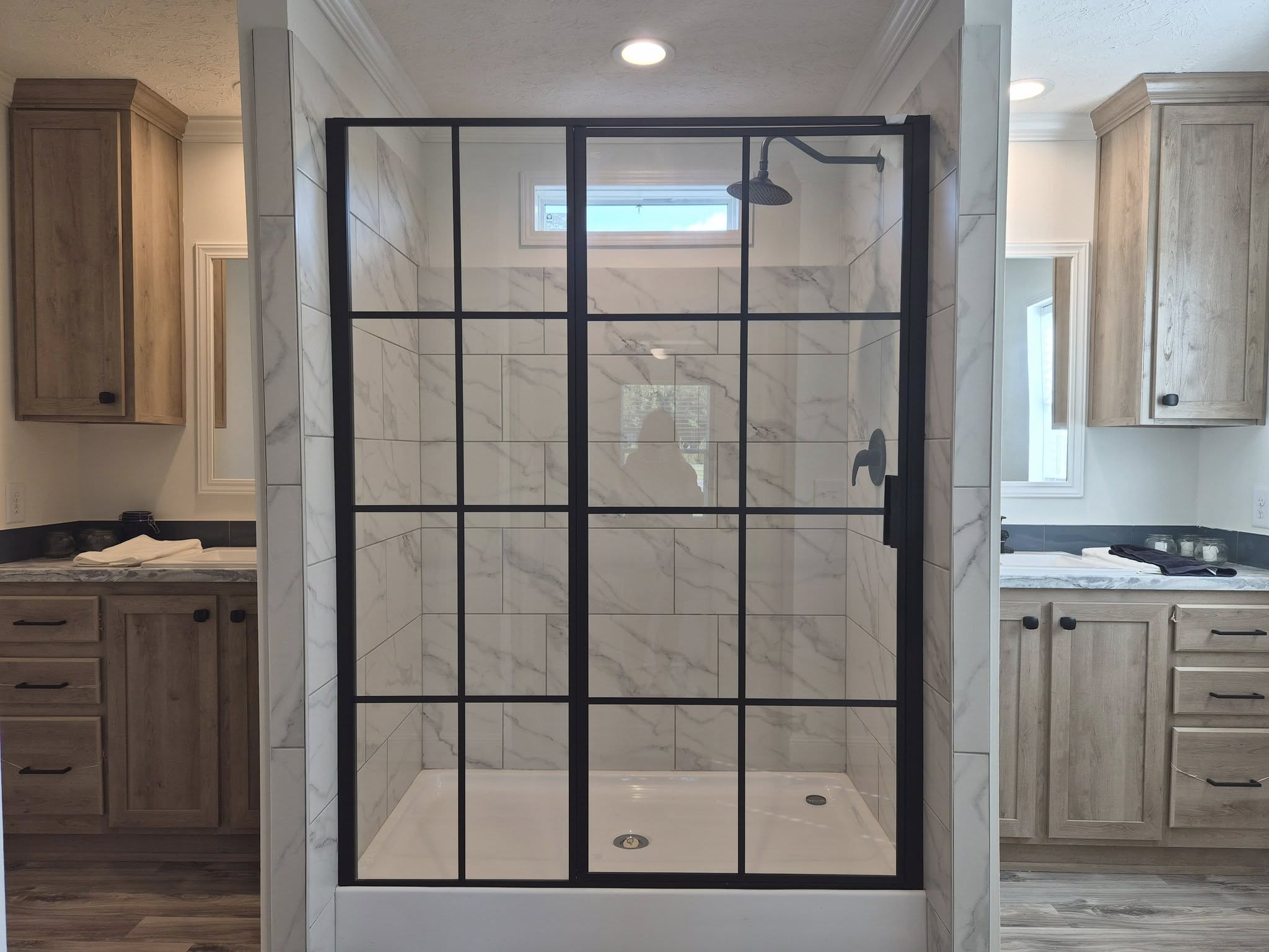 Modern bathroom with a walk-in shower featuring black metal frames and white marble tile. Wooden cabinets flank the shower, creating a cozy, elegant ambiance.