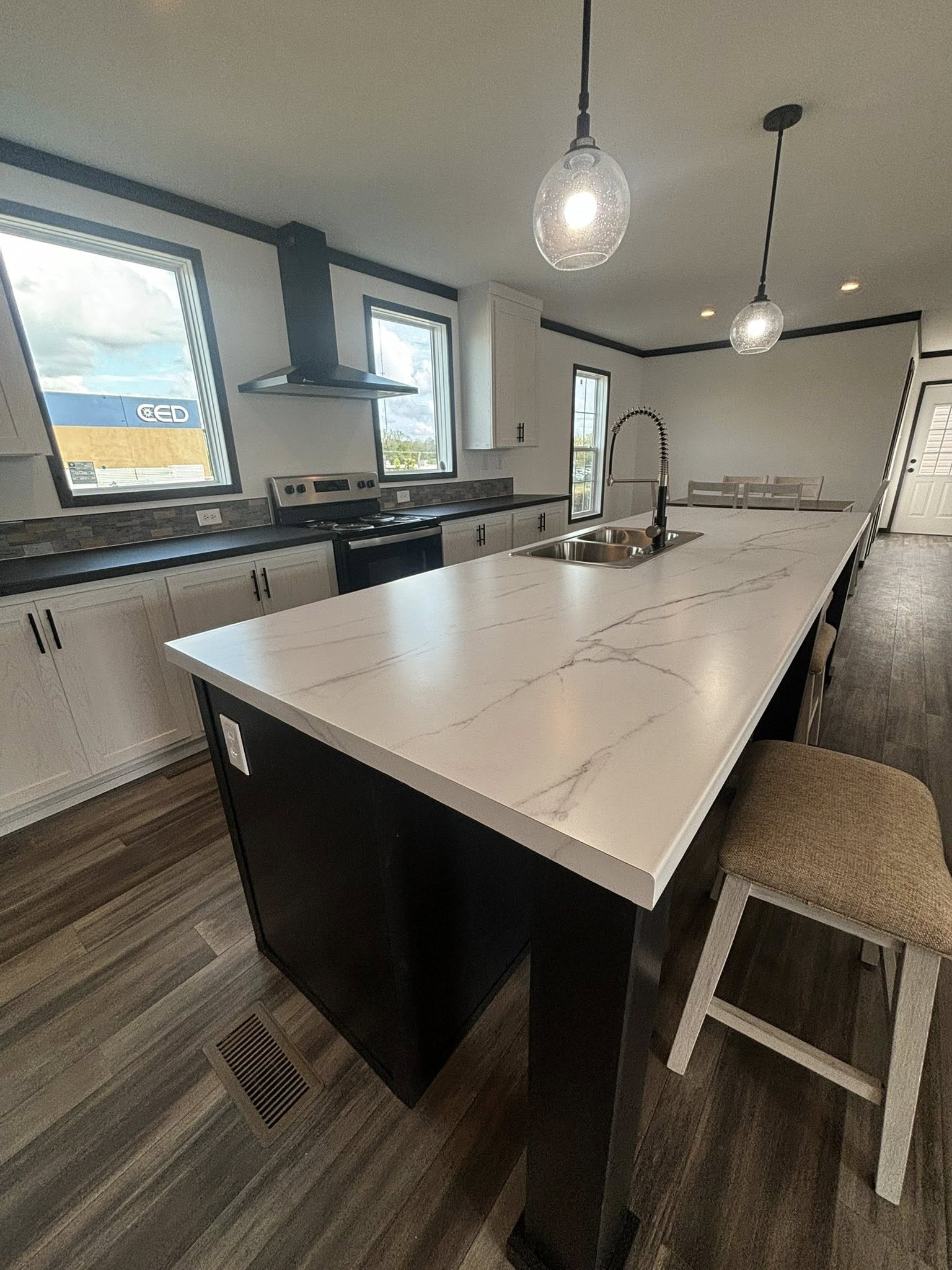 Modern kitchen with a large white marble island, black cabinets, and pendant lights. Bright, airy atmosphere with wooden floor and stainless steel accents.