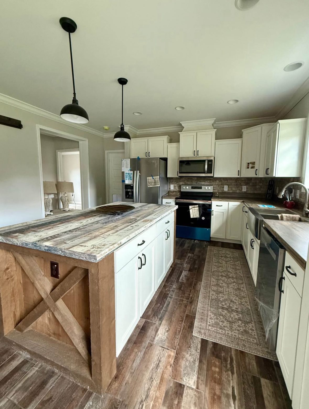 Rustic kitchen with a large, wooden island, industrial pendant lights, white cabinets, and stainless steel appliances. Warm, cozy ambiance.