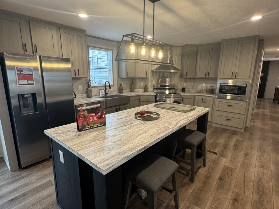 Modern kitchen with gray cabinets, stainless steel appliances, and a wooden floor. A marbled island with barstools is lit by hanging bulbs. Cozy and inviting atmosphere.