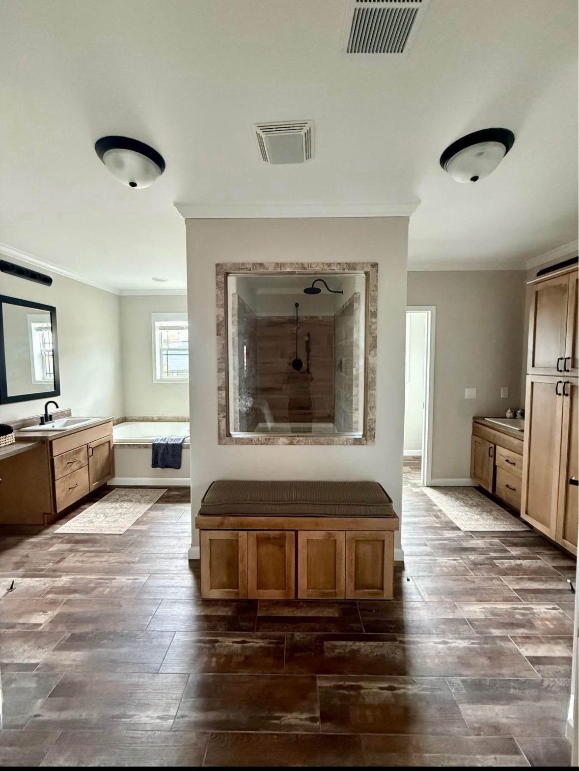 Spacious bathroom with wooden cabinets, tile flooring, and a central glass shower. A tub is on the left, creating a calm and modern atmosphere.