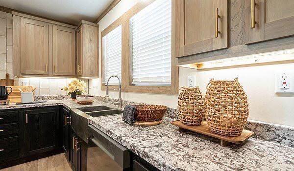 Modern kitchen with a marble countertop, stainless steel sink, light wood cabinets, and large baskets. Soft lighting creates a warm, inviting atmosphere.