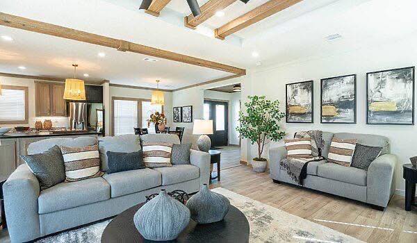 Modern living room with gray sofas and striped pillows, wooden beams on the ceiling, a round coffee table, abstract wall art, and a cozy ambiance.