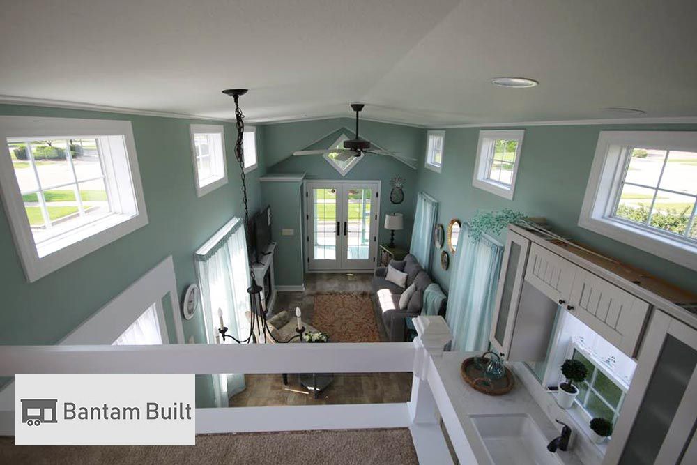 A cozy, bright living room with teal walls and large windows, featuring a gray couch and a pastel rug. Natural light and soft colors create a serene atmosphere.