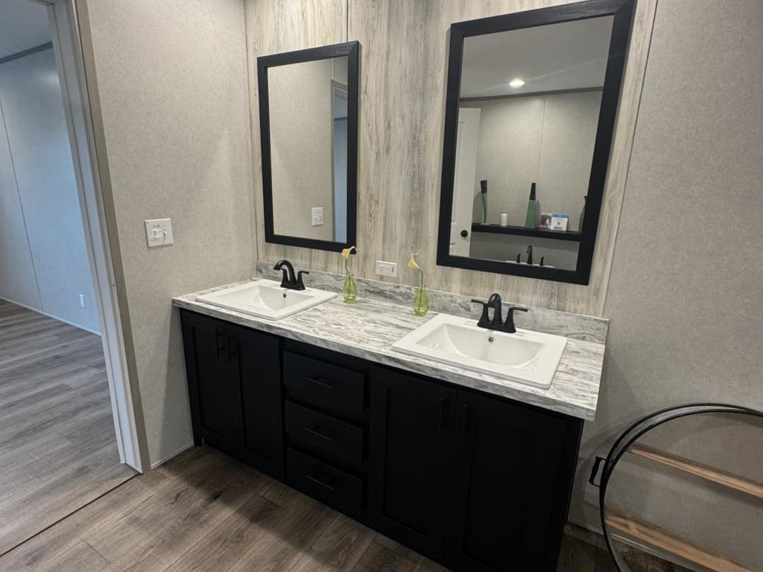 Modern bathroom showcasing a dual-sink vanity with black cabinetry, marble countertop, two rectangular mirrors, and minimalistic decor on a wooden floor.