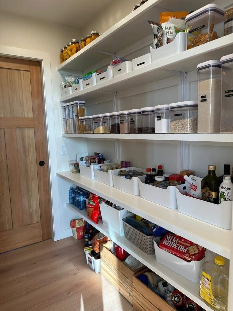 A neatly organized pantry with white shelves displaying labeled containers of food items, bottles, and jars, creating a clean and orderly atmosphere.
