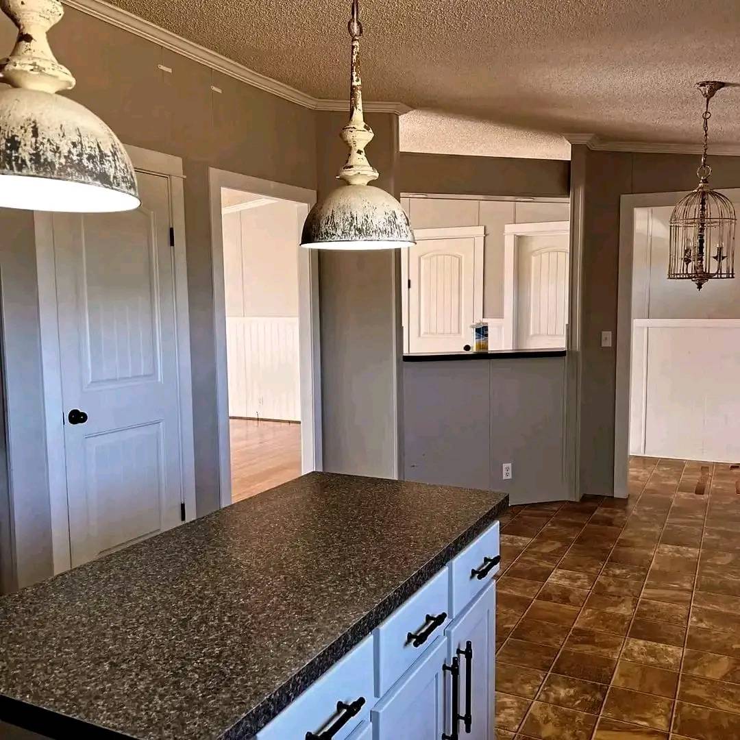 Modern kitchen with a granite countertop island, white cabinets, and vintage-style hanging lights. The space feels warm and inviting with neutral tones.