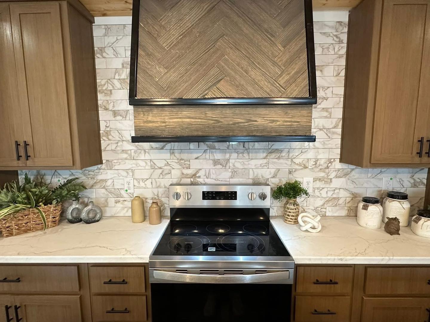 Modern kitchen with stainless steel stove, marble backsplash, and wooden cabinets. Decor includes plants and jars on white countertops.