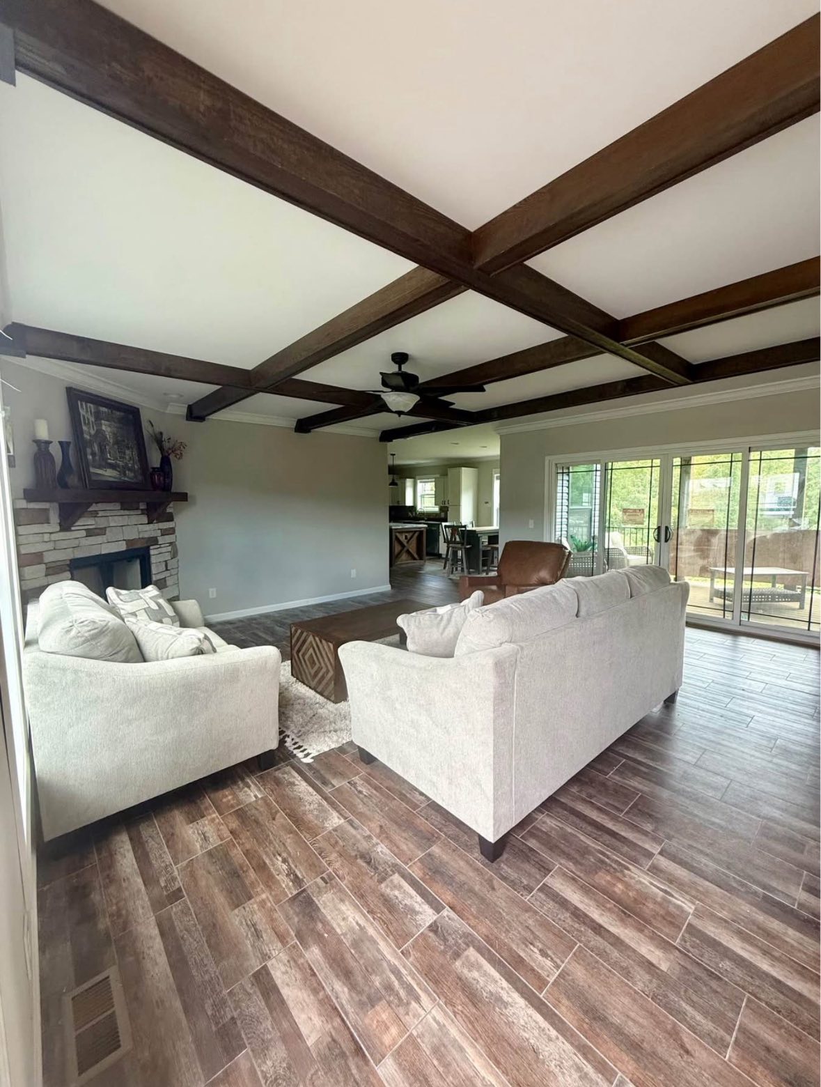 Spacious living room with beige sofas, a brick fireplace, wooden ceiling beams, and sliding glass doors opening to a patio. Cozy and inviting atmosphere.