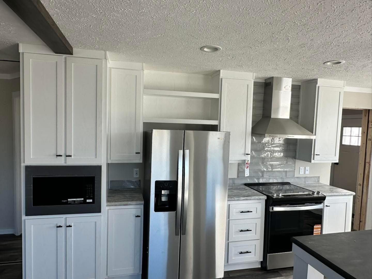 Modern kitchen with white cabinets, stainless steel appliances, including a fridge, oven, and microwave. Features marble countertops and a sleek range hood.