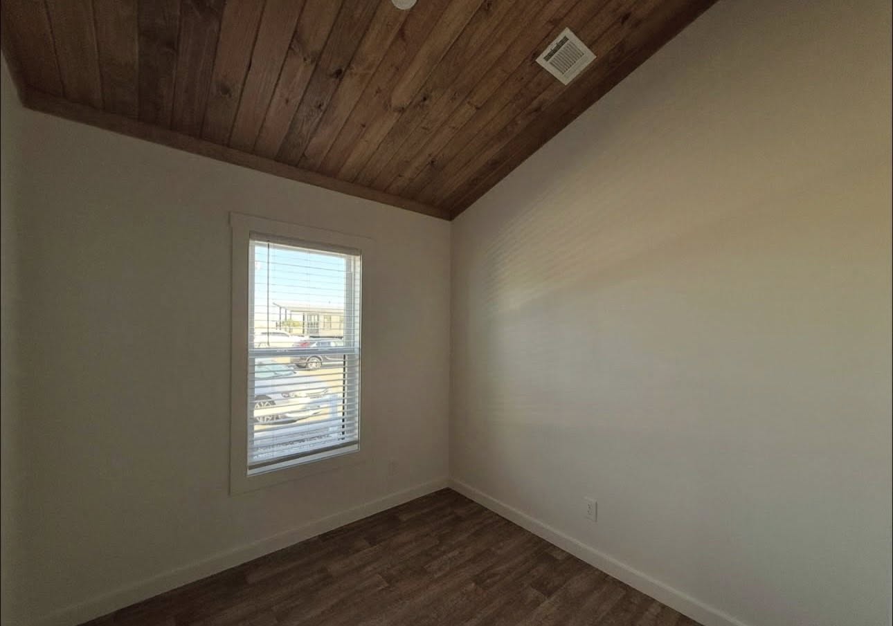 Small room with white walls, featuring a wooden ceiling and floor. A window with blinds lets in natural light, creating a calm, minimalist atmosphere.