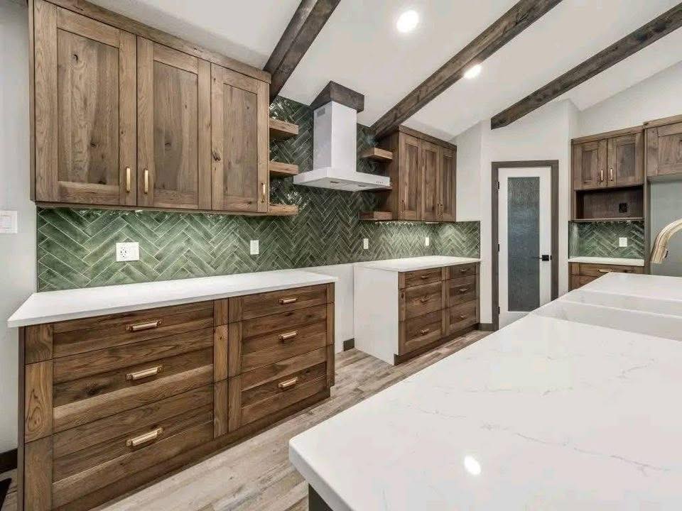 Rustic kitchen with wooden cabinets, white countertops, and green herringbone tile backsplash. Exposed wooden beams add warmth and charm.