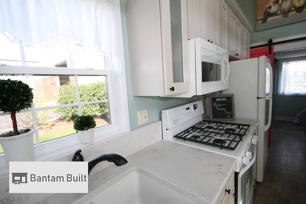 Bright, modern kitchen with white cabinets, gas stove, and microwave. Light pours in through a window above a potted plant. Cozy, inviting atmosphere.