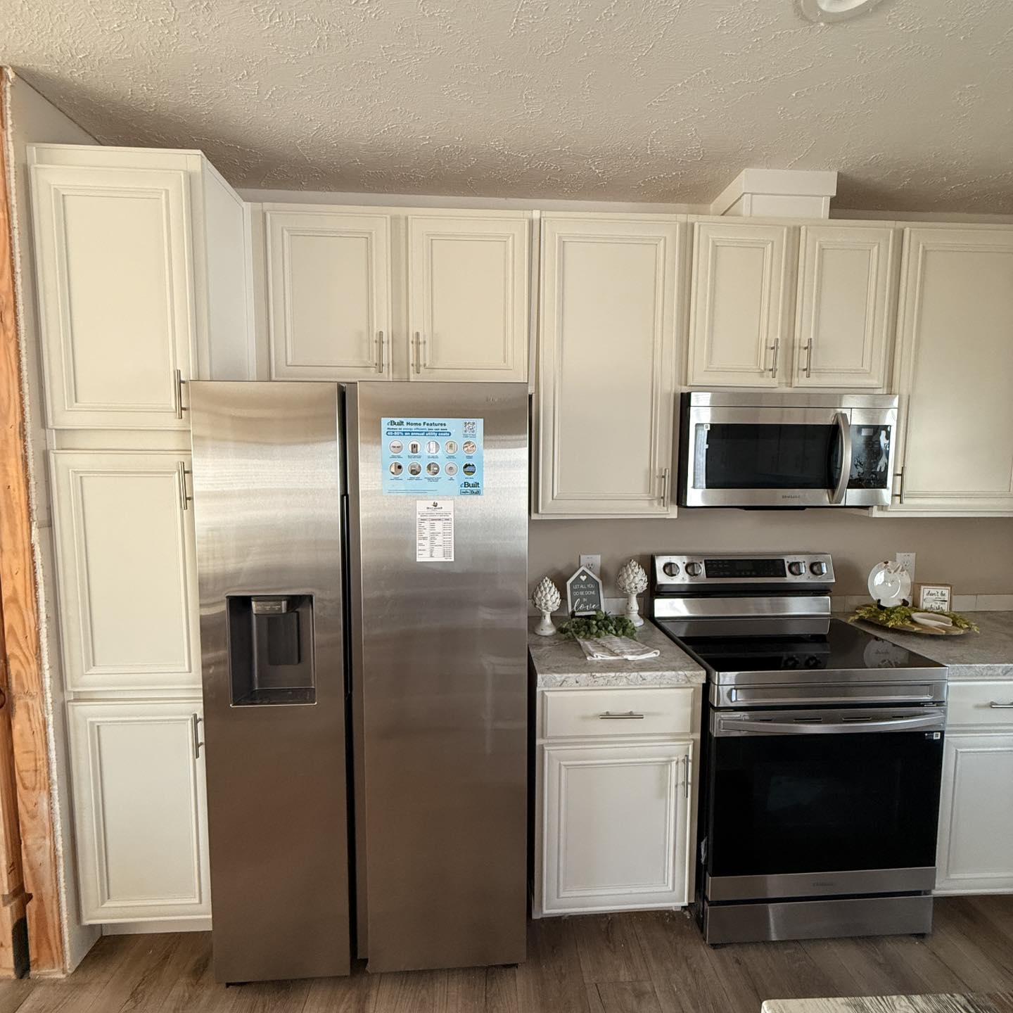 Modern kitchen with stainless steel fridge, microwave, and oven. White cabinets, marble countertop, and decorative items create a cozy, clean ambiance.