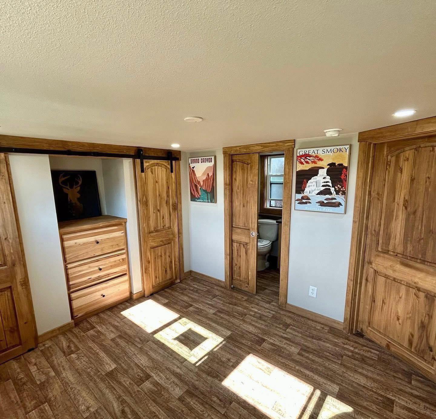 Cozy bedroom with wooden flooring and doors. A dresser sits between sliding closet doors. Two nature-themed posters adorn the light walls.