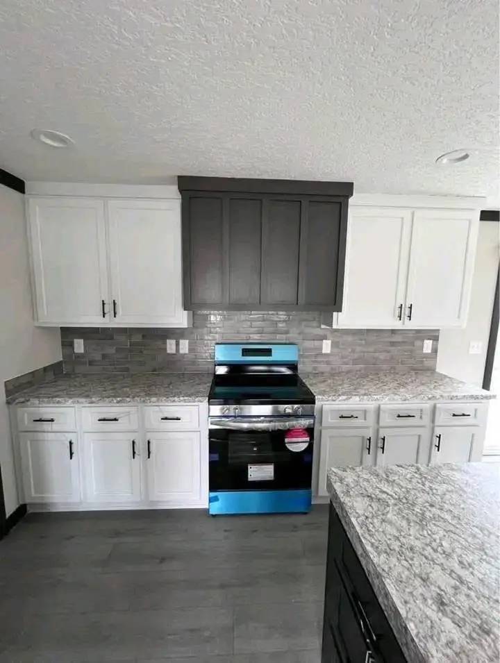 Modern kitchen with gray and white cabinetry, a stainless steel oven with blue accents, speckled countertops, and a gray tiled backsplash.
