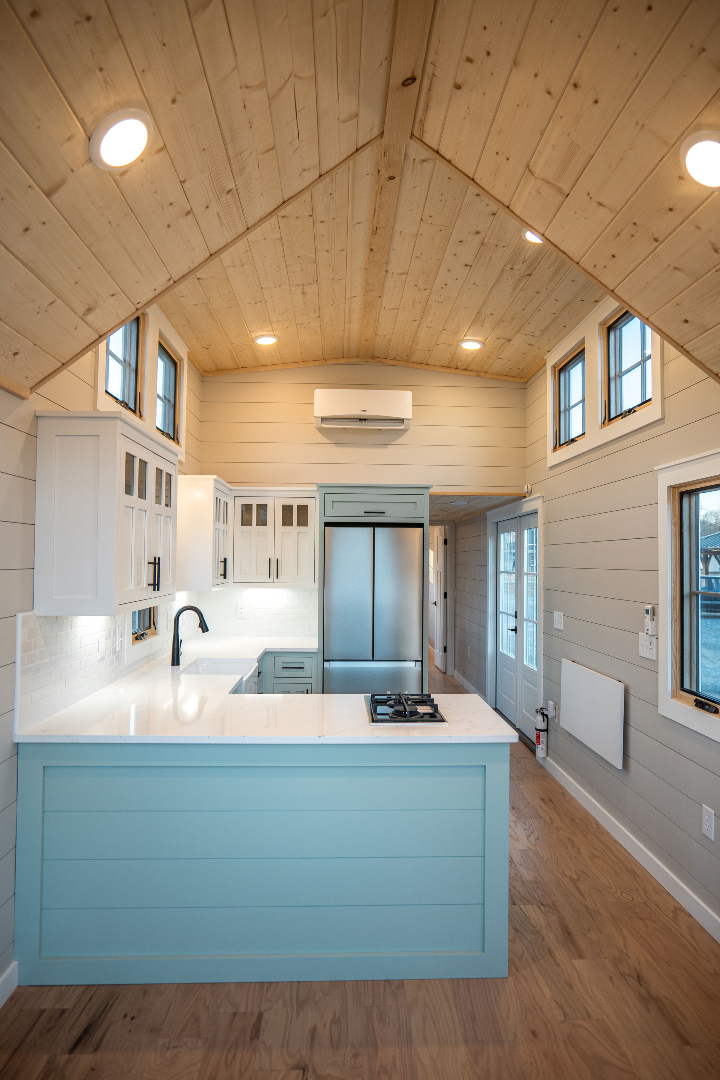 Cozy kitchen with vaulted wooden ceiling, pale blue island, white cabinets, stainless steel appliances, and ambient recessed lighting.