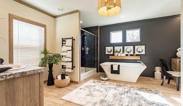 Spacious bathroom with modern decor. Features a freestanding tub, black accent wall, shower, and wooden flooring. Natural light and tranquil ambiance.