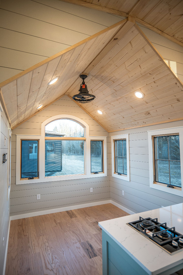 Bright, cozy room with a wood-paneled, vaulted ceiling. Four large windows let in natural light. A gas stove is set on a white countertop. Rustic charm.