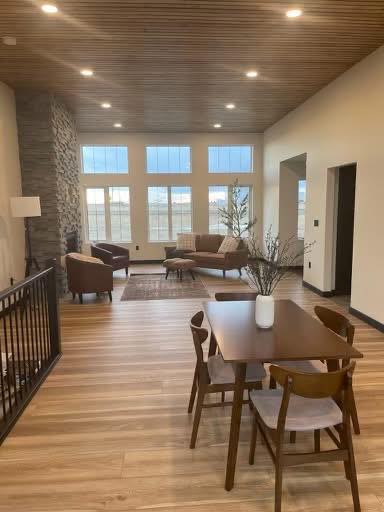 Spacious living room with wooden floors, modern dining set, and cozy seating by a stone fireplace. Large windows offer natural light and outdoor views.